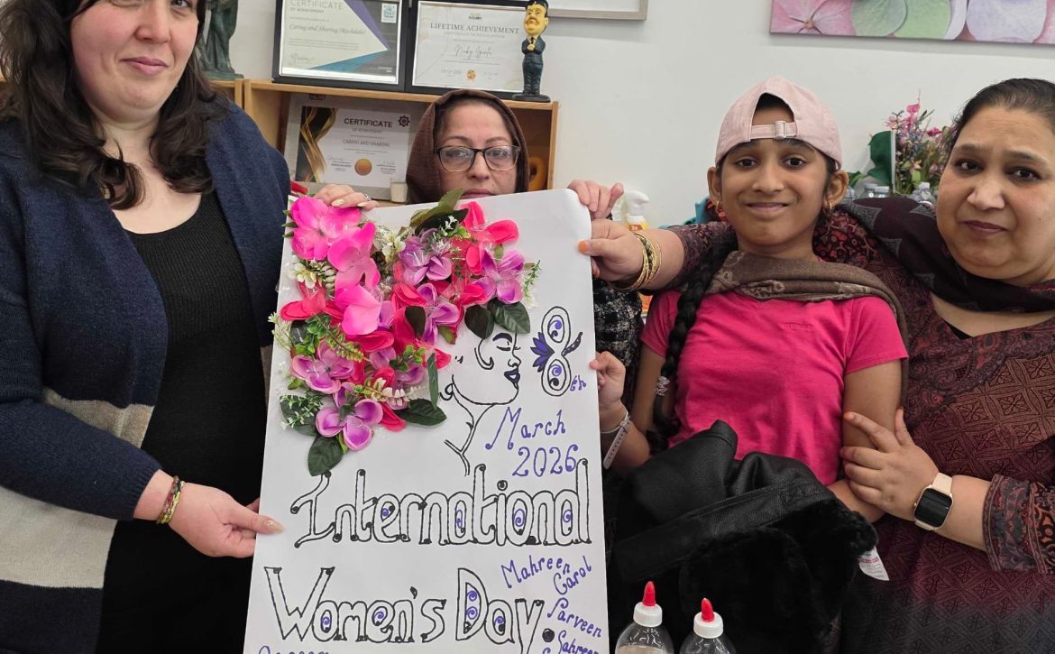 Participants at Caring and Sharing Rochdale proudly display a collaborative floral poster for International Women's Day 2026, symbolizing the #GiveToGain theme through community art.