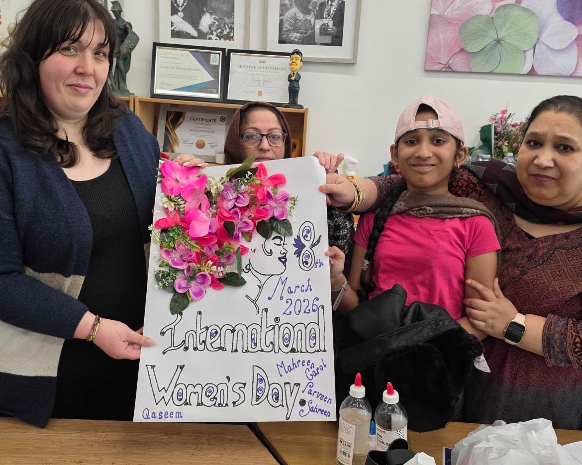 Participants at Caring and Sharing Rochdale proudly display a collaborative floral poster for International Women's Day 2026, symbolizing the #GiveToGain theme through community art.