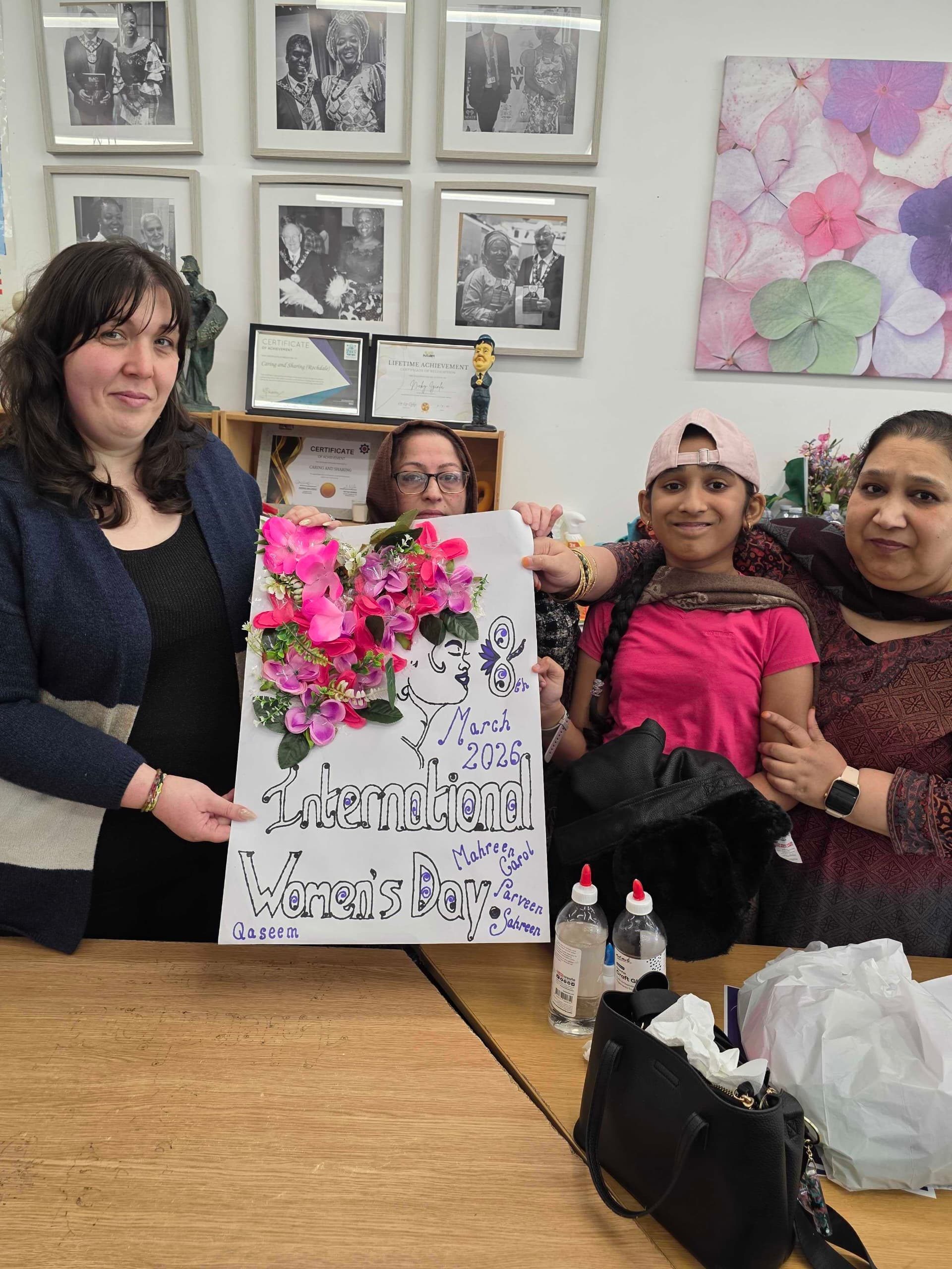Participants at Caring and Sharing Rochdale proudly display a collaborative floral poster for International Women's Day 2026, symbolizing the #GiveToGain theme through community art.