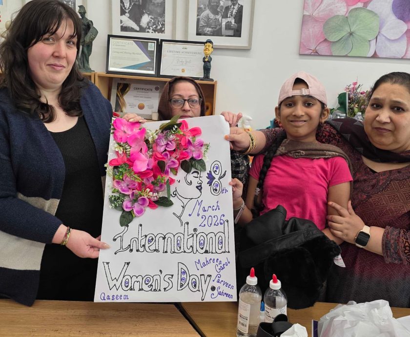Participants at Caring and Sharing Rochdale proudly display a collaborative floral poster for International Women's Day 2026, symbolizing the #GiveToGain theme through community art.