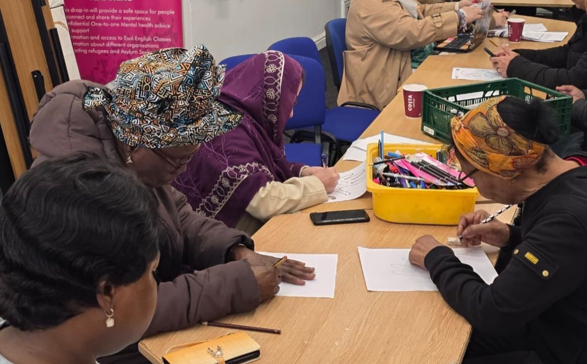 Women participating in a community activity at CAS with a backdrop referencing refugees and asylum seekers