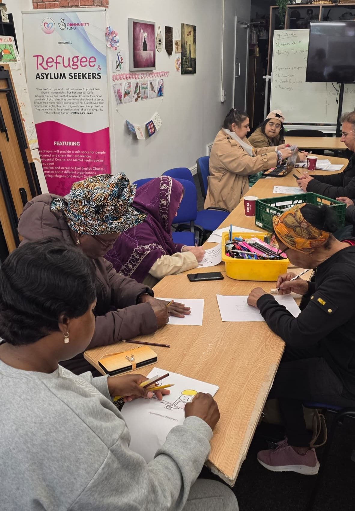 Women participating in a community activity at CAS with a backdrop referencing refugees and asylum seekers
